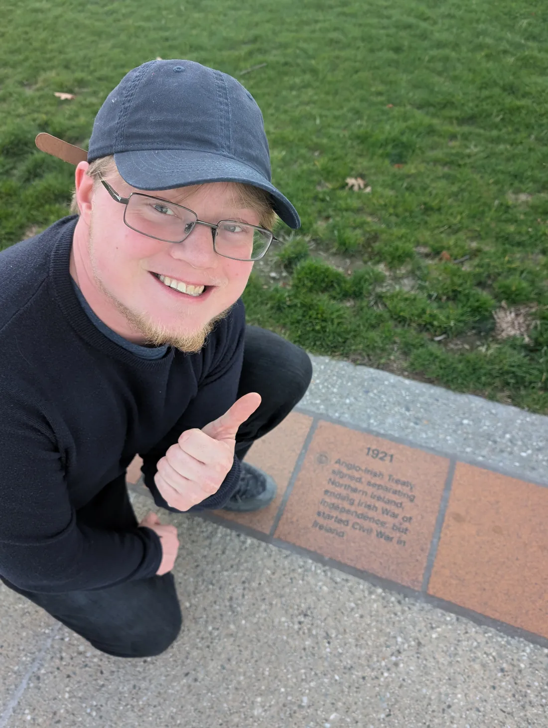 Jamie Cras giving a thumbs up beside a commemorative stone marking the 1921 Anglo-Irish Treaty